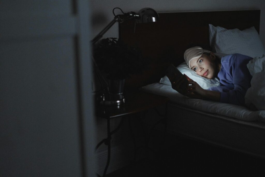 A woman in bed using a smartphone at night, her face illuminated by the screen's light.